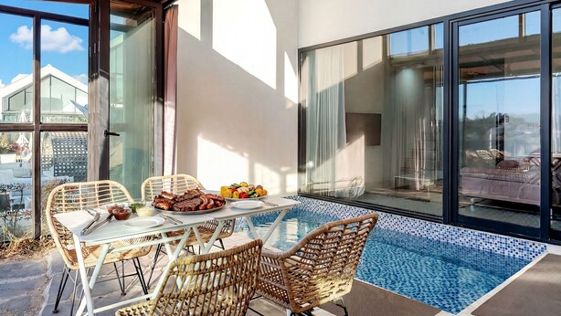 Un área de comedor al aire libre con sillas de mimbre y una mesa lista para una comida, con vista a una piscina.