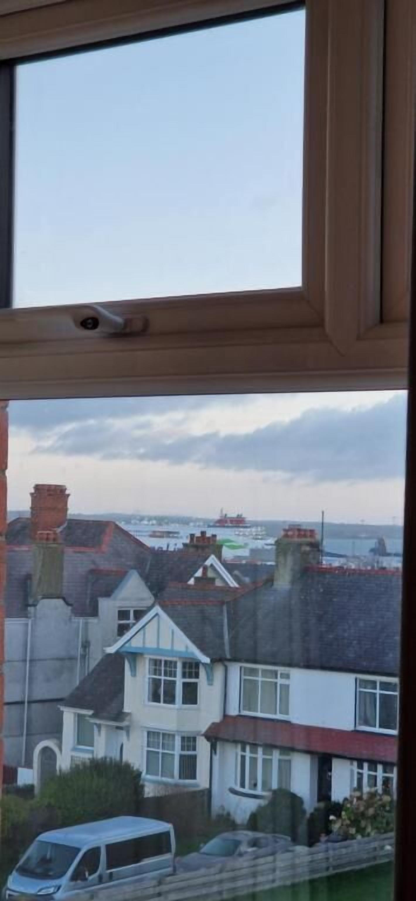 Vista a través de una ventana de una zona residencial con casas, una furgoneta estacionada y una masa de agua al fondo.