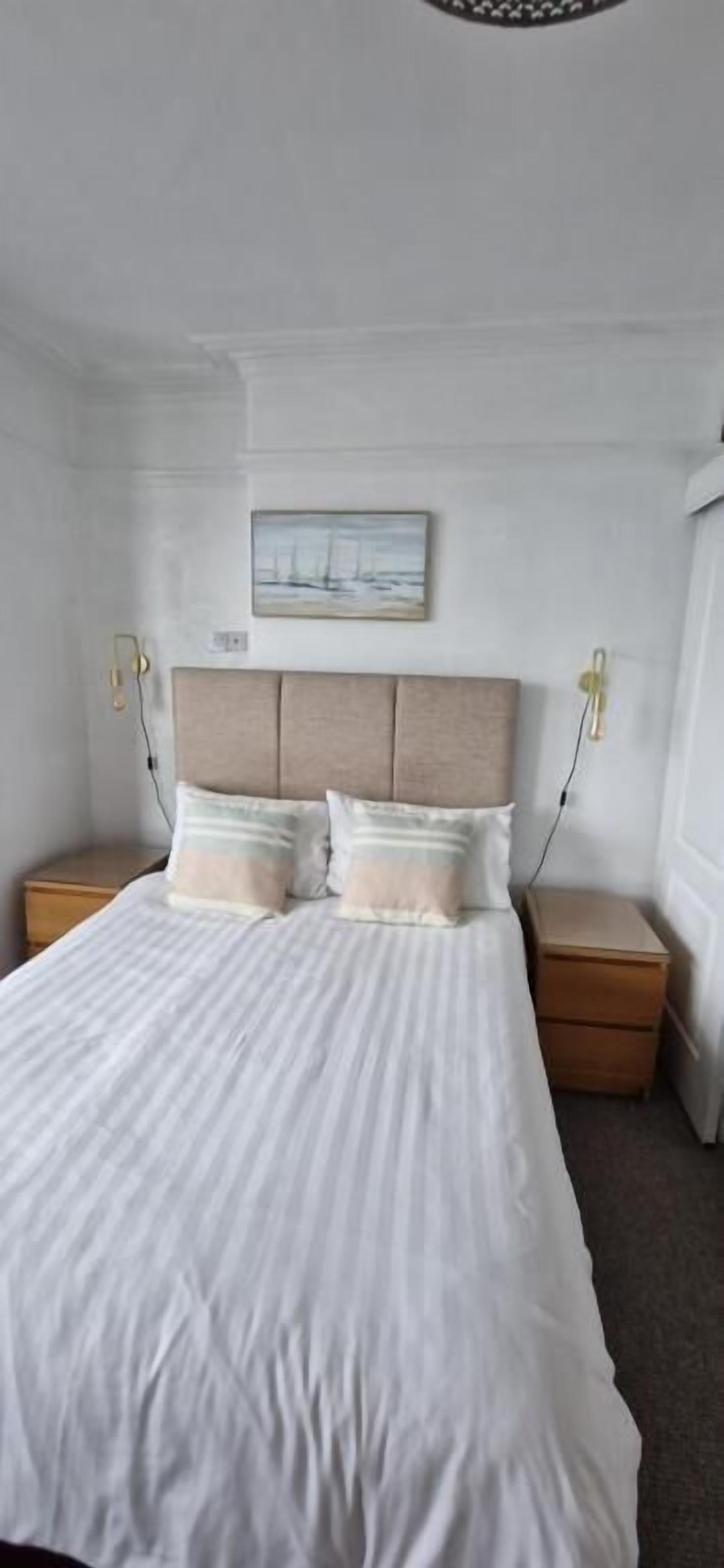 Un lit bien fait, avec une tête de lit, deux tables de chevet et un tableau accroché au mur.