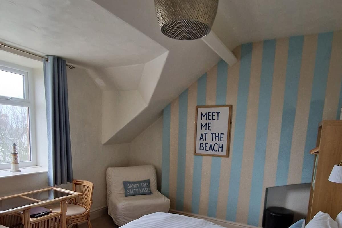 A bedroom with a bed, a desk, a chair, a window, and a wall with a striped pattern.