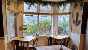 A dining area with a wooden table and chairs, large windows with curtains, and a ceiling fan. - Black Sheep Lodge (Holyhead)