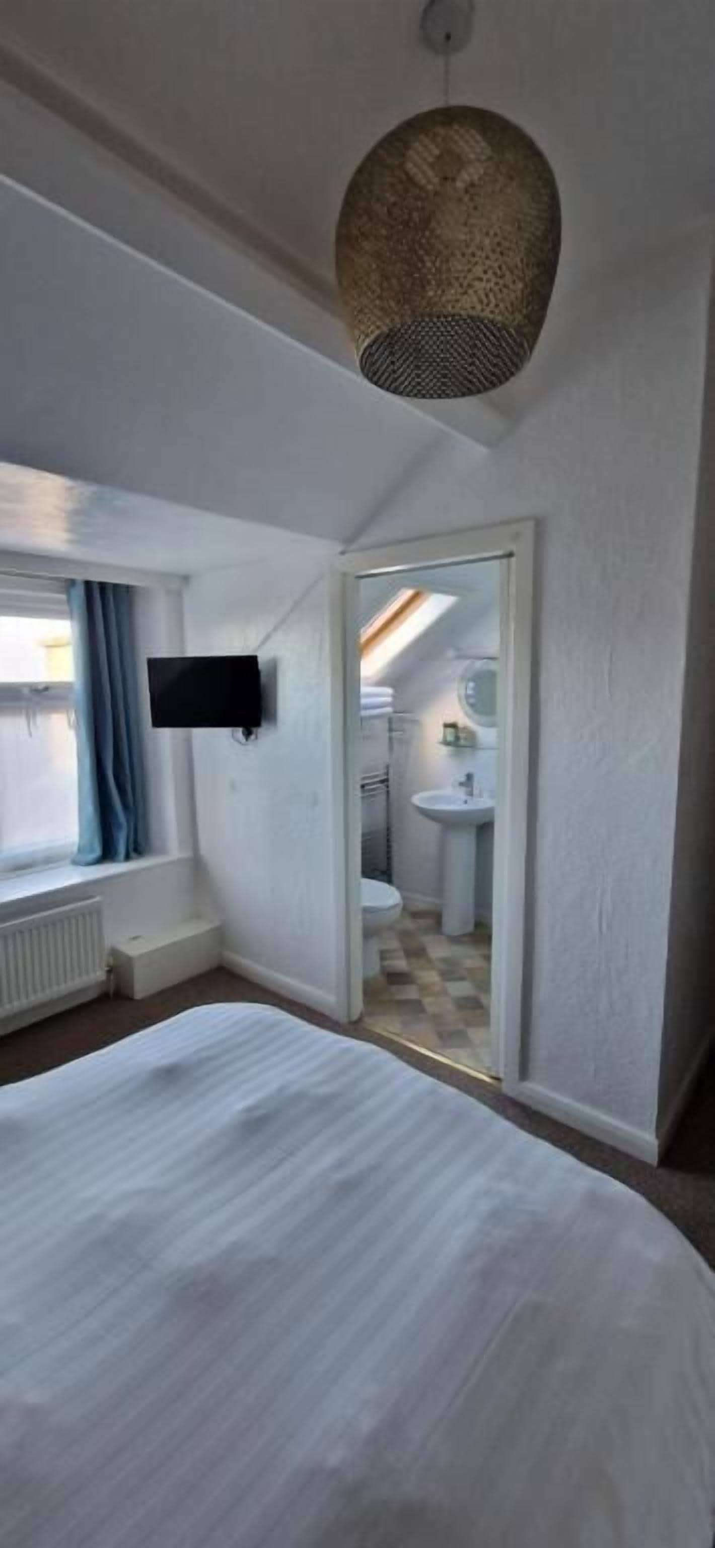 A bedroom with a bed, a television, a window with curtains, and a bathroom visible through an open door.