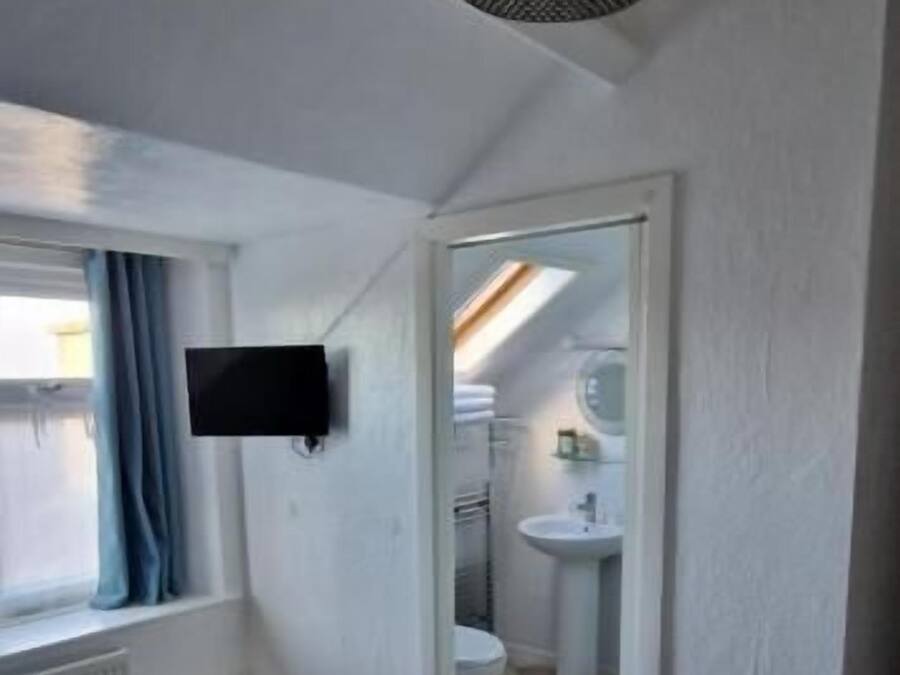A bedroom with a bed, a television, a window with curtains, and a bathroom visible through an open door.