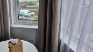 A room with a large window, a table with a tissue box, and curtains. - Black Sheep Lodge (Holyhead)