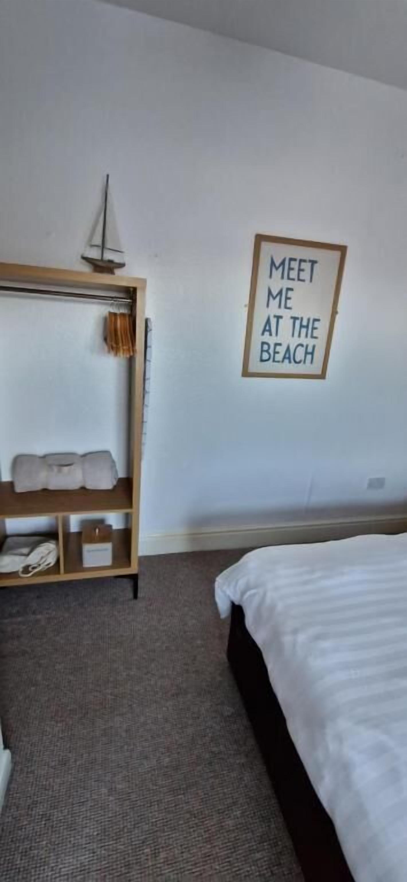 Quarto de hotel com cama, prateleira de madeira com toalhas e um quadro na parede.