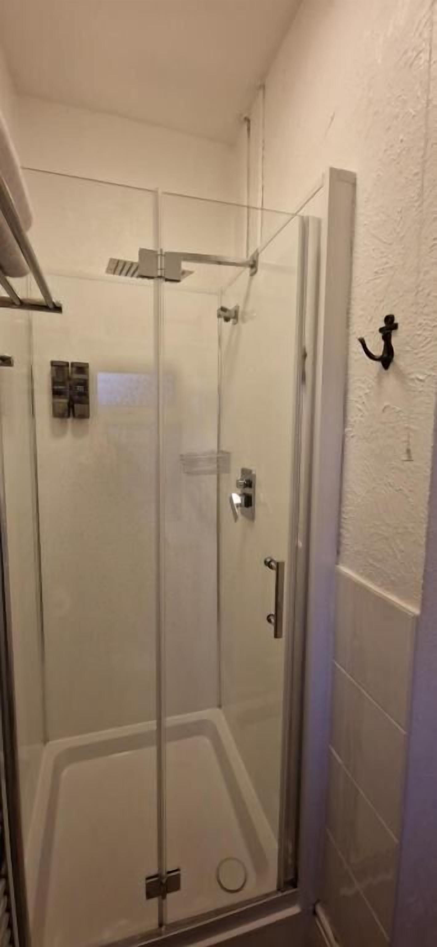 Cabina de ducha con paredes de vidrio, una puerta, un perchero y una lámpara fijada a la pared.