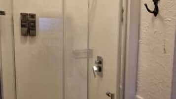 Cabina de ducha con paredes de vidrio, una puerta, un perchero y una lámpara fijada a la pared.
