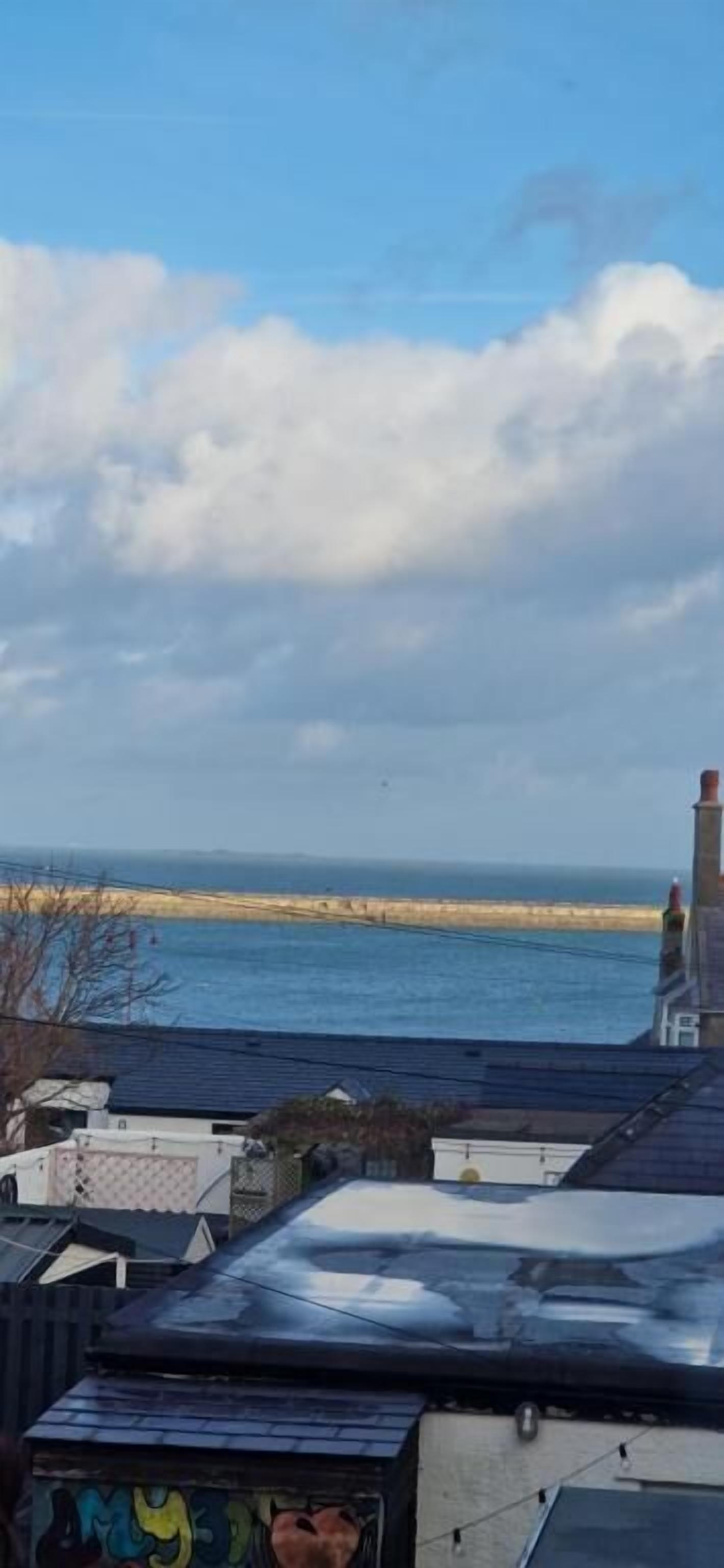 Blick auf die Küste mit einer Hafenmauer und Gebäuden im Vordergrund.