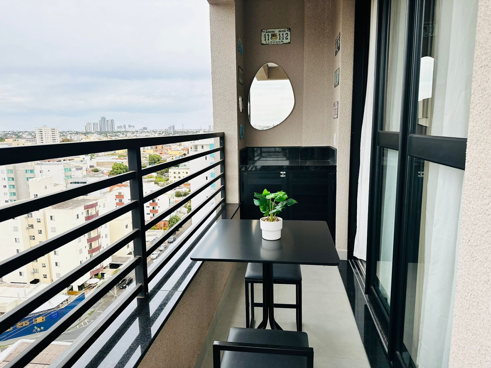 A balcony with a table and chairs, a potted plant, a mirror, and a view of the cityscape.