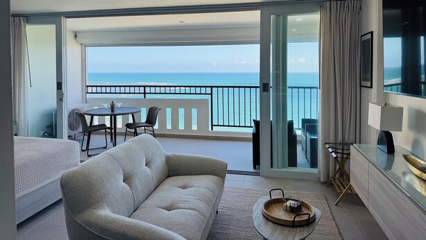 A modern hotel room with a balcony, a sofa, a dining table, and a TV. - -- NEW -- Paradise & Luxury II Seaside Sanctuary Ocean Views & Fully Renovated (Luquillo)