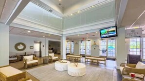 Eine geräumige Lobby mit hohen Decken, gemütlichen Sitzbereichen und einem großen Fernsehbildschirm.