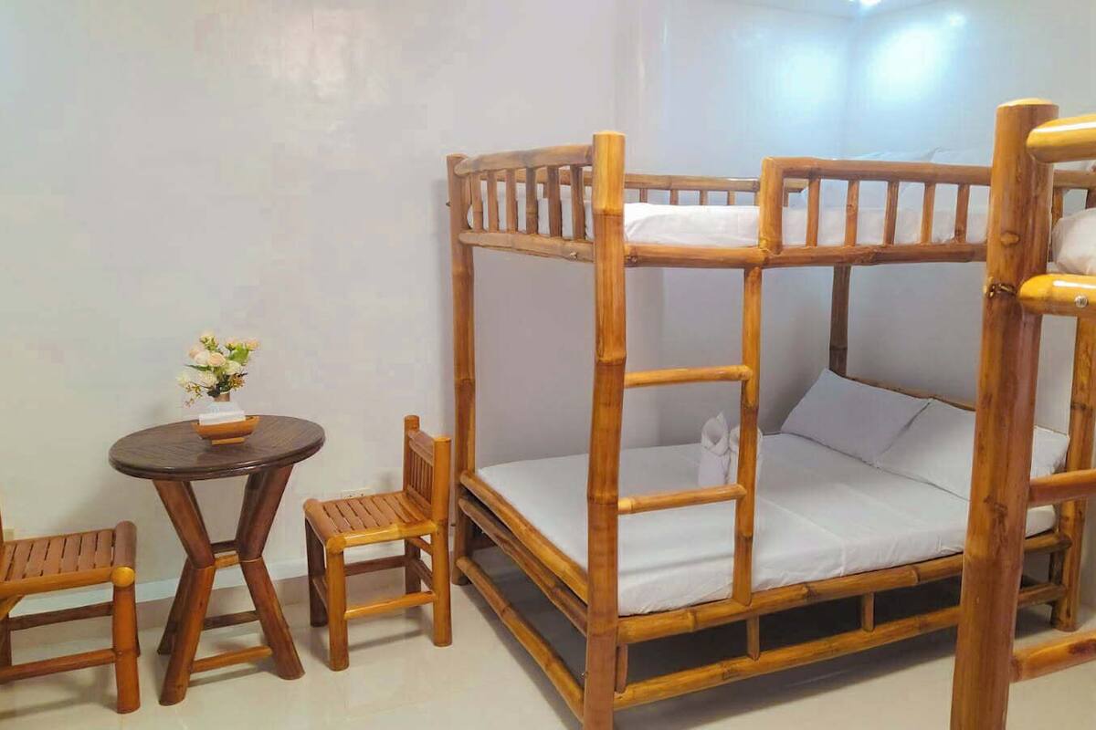 A wooden bunk bed with a small table and two chairs in a room with white walls.