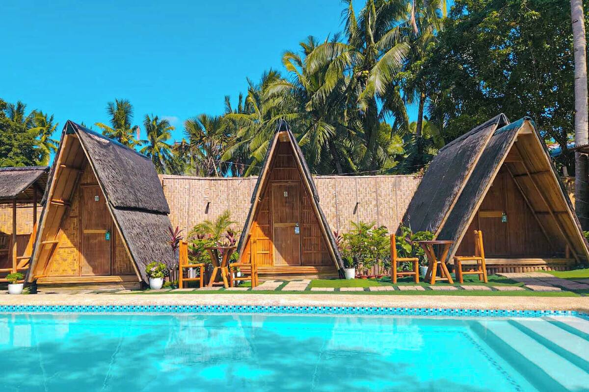 A poolside area with thatched-roof huts and a clear blue pool.