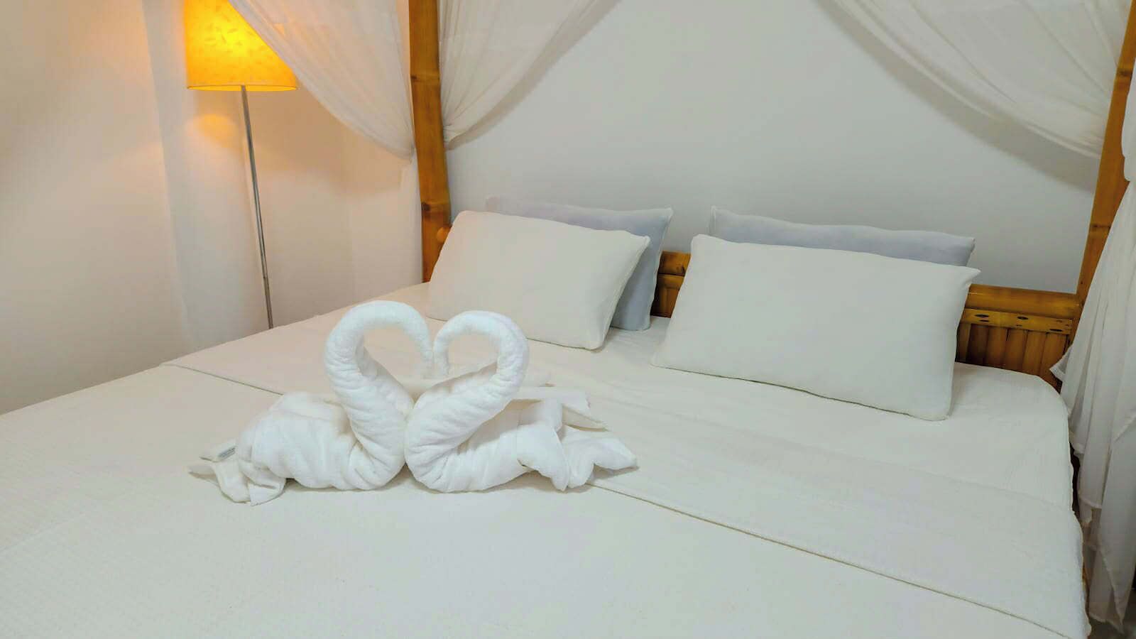 Une chambre d’hôtel avec un lit bien fait, une literie blanche et un lit à baldaquin.