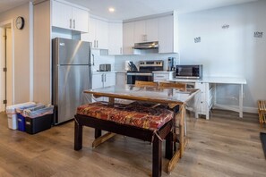 A modern kitchen with white cabinets, stainless steel appliances, and a wooden dining table with a patterned bench.