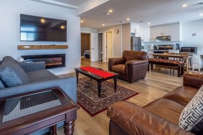 Ein Wohnzimmer mit einer Couch, einem Couchtisch, einem Kamin, einem Fernseher und einer Küchenzeile mit Schränken und Geräten.
