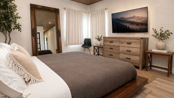 A bedroom with a large bed, wooden dresser, and a painting of a mountain landscape.
