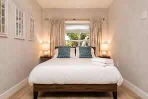 A bedroom with a wooden bed, two bedside lamps, a window with curtains, and a view of greenery outside. - Burbank Getaway (Burbank)