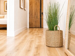 A wicker basket with green plants on a wooden floor, a wooden door, and a white wall with framed pictures. - Burbank Getaway (Burbank)