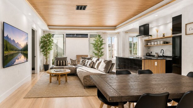 A modern living room with a wooden ceiling, a large TV, a sofa, a dining table, and a kitchen area.