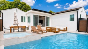 A swimming pool with lounge chairs and a table, surrounded by a white building with large windows and a door.