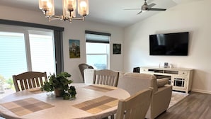 Un comedor con una mesa redonda, sillas, una planta en maceta, un ventilador de techo y un televisor fijado a la pared.