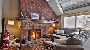 A cozy living room with a brick fireplace, a sofa, a coffee table, and a fireplace mantle with decorations. - Sunrise Timberline 3BR ski in/ski out with fireplace, pool and hot tub (Killington)