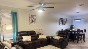 Ein Wohnzimmer mit einem dunkelbraunen Ledersofa, einem kleinen Couchtisch und einem Essbereich mit Tisch und Stühlen.
