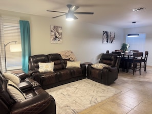 A living room with a dark brown leather sectional sofa, a small coffee table, and a dining area with a table and chairs. - Austin Hotspot - Minutes to Airport, Downtown & F1 (Austin)