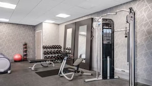 Une salle de sport équipée de divers appareils, notamment un banc de musculation, un rameur et un mur rempli d’haltères.