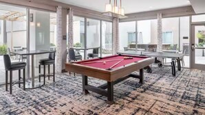 Une table de billard dans une pièce dotée de grandes fenêtres, d’un coin repas et d’un tapis à motifs.