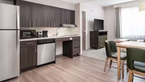 Une cuisine moderne avec des meubles de couleur bois foncé, des appareils en acier inoxydable et un coin repas comprenant une table et des chaises en bois.
