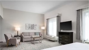 Une chambre d’hôtel comprenant un lit, un canapé, une chaise, une télévision, une commode et une fenêtre avec des rideaux.
