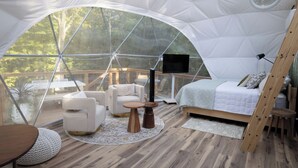 Une tente en forme de dôme comprenant un lit, un coin salon et un téléviseur.