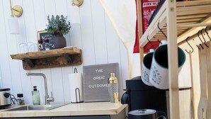 Une cuisine avec un plan de travail en bois, un évier, un porte-tasses suspendu et un panneau accroché au mur.