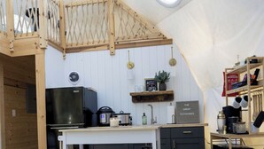 Un espace de vie confortable et bien éclairé, aménagé comme une tente, avec un coin cuisine, des meubles en bois et une échelle de corde suspendue.