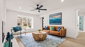 A spacious living room with a large window, a ceiling fan, a wooden coffee table, a sofa with cushions, and a blue patterned rug. - Fully Renovated Furnished Home in Hurst – Perfect for Mid-Term Stays (Hurst)