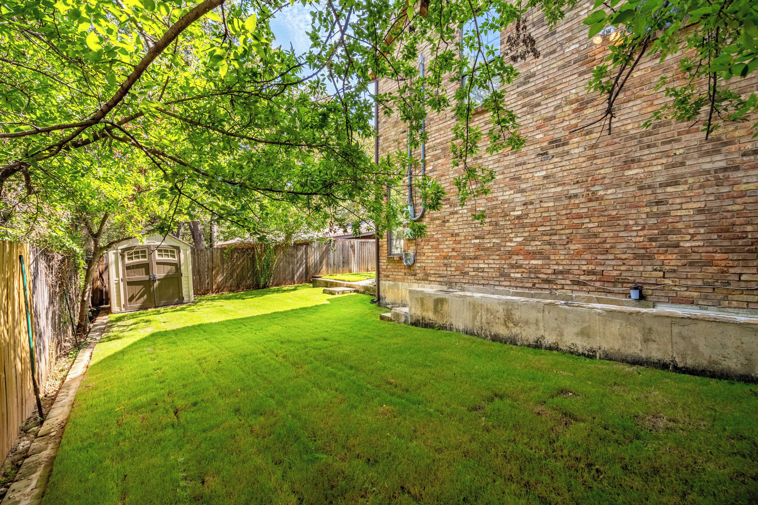 A backyard with a brick wall, a wooden fence, and a well-maintained lawn.