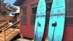 Two surfboards leaning against a red building with a wooden staircase leading to a deck. - Cozy 3-bedroom cabin in adorable Gimli, Manitoba (Gimli)