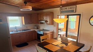 A kitchen with wooden cabinets, a stainless steel refrigerator, a sink, and a dining table with chairs.