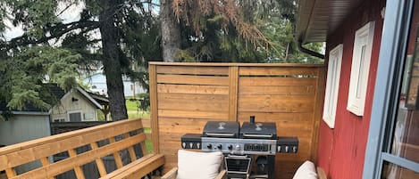 Terraza exterior con mobiliario de madera, incluyendo un sofá y sillas, y una parrilla.