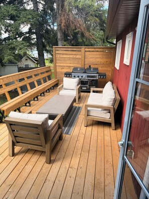 Een terras buiten met houten meubels, waaronder een bank en stoelen, en een barbecue.