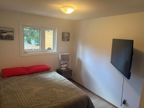 Une chambre à coucher avec un lit, une fenêtre, un téléviseur fixé au mur et une lampe de chevet.