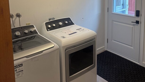 A laundry room with a washer and dryer, a door with a window, and a black doormat.