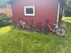 Een rood gebouw met een raam en een deur, een houten omheining, en een gazon met vier fietsen er tegen aangeleund.