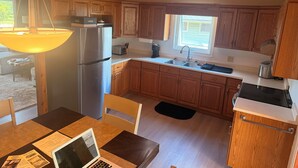 A kitchen with wooden cabinets, a stainless steel refrigerator, a sink, and a dining table with a laptop. - Cozy 3-bedroom cabin in adorable Gimli, Manitoba (Gimli)