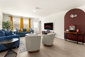 Ein modernes Wohnzimmer mit einem blauen Sofa, einem weißen Sessel, einem Couchtisch und einem an der Wand befestigten Fernseher.