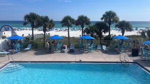 Ein Poolbereich mit blauen Sonnenschirmen, Liegestühlen und Blick auf Strand und Meer.