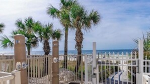 Ein verschlossenes Tor mit Palmen, ein Holzboden und Blick auf Strand und Meer.