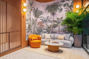 Una sala de estar moderna con un sofá, una mesa de centro redonda, un separador de madera y un gran mural en la pared con plantas tropicales.